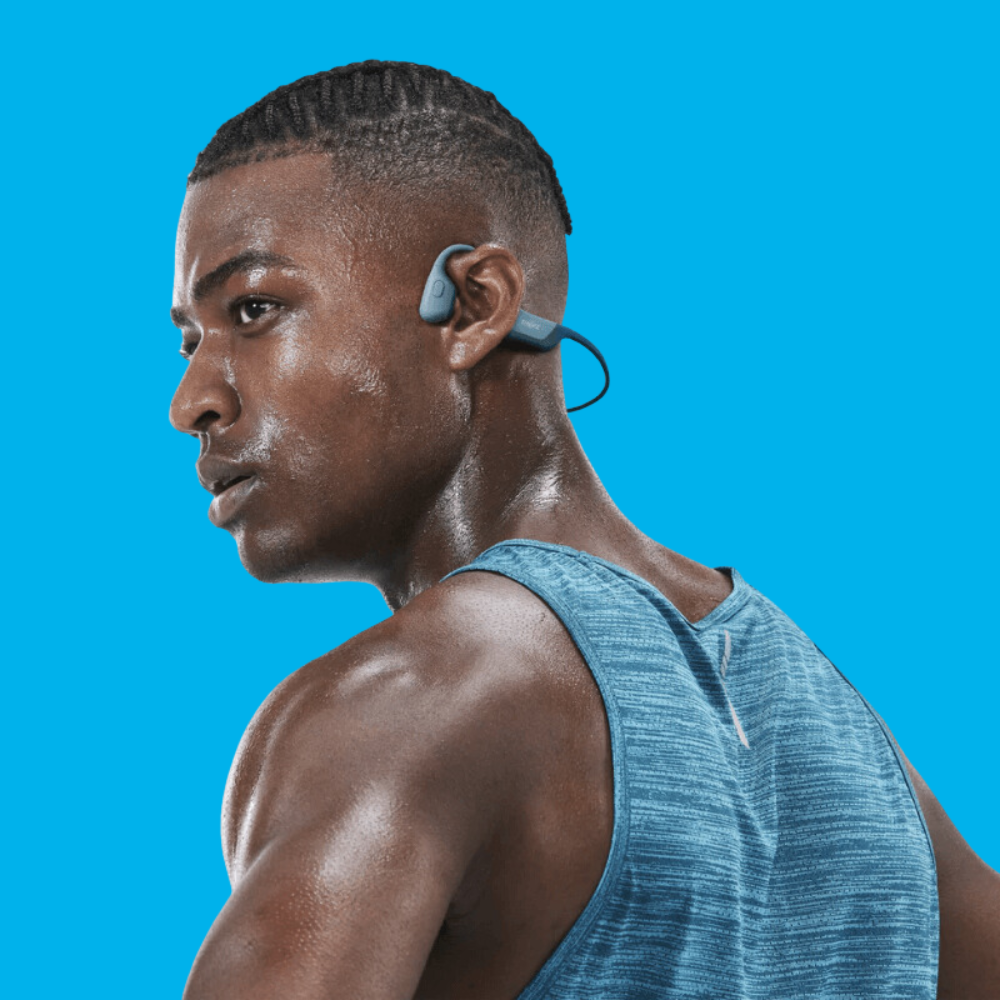 A young man wearing Shokz OpenRun sport headphones on a blue background.
