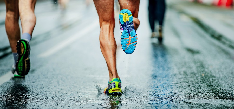 A group of runners legs and feet hitting a rainy roadway